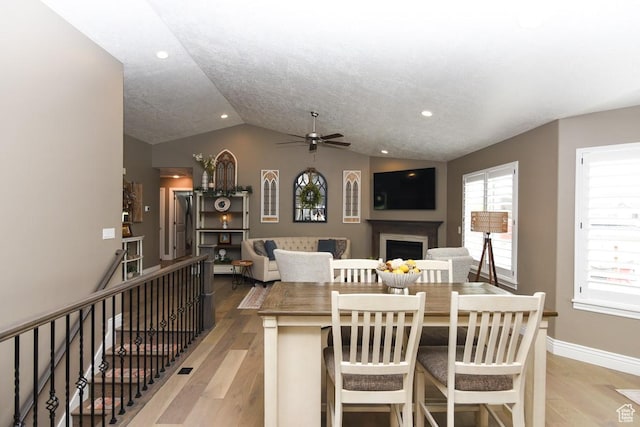 dining space featuring vaulted ceiling, light wood-style floors, a ceiling fan, a fireplace, and baseboards