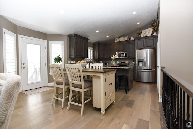 kitchen featuring appliances with stainless steel finishes, a center island, dark brown cabinetry, a kitchen breakfast bar, and light wood-type flooring