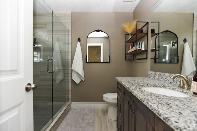 bathroom with a shower stall, baseboards, vanity, a textured ceiling, and toilet