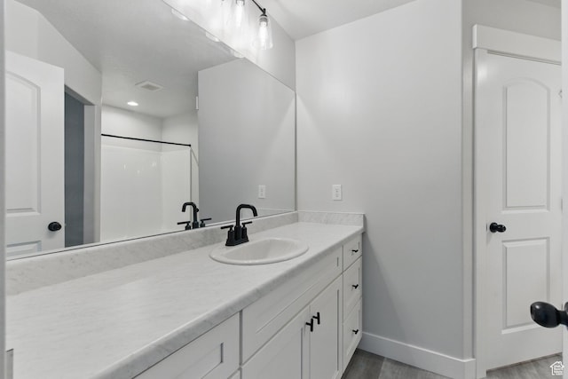 bathroom featuring baseboards, wood finished floors, vanity, a shower, and recessed lighting