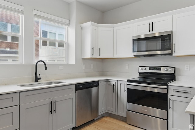 kitchen with appliances with stainless steel finishes, a sink, light countertops, light wood-style floors, and white cabinetry
