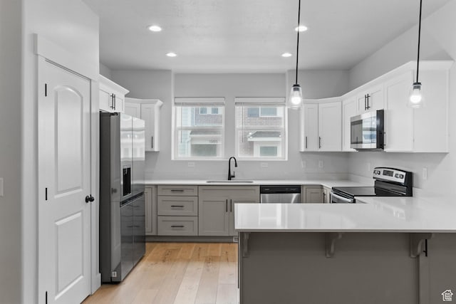 kitchen with stainless steel appliances, a sink, a peninsula, light wood-type flooring, and recessed lighting