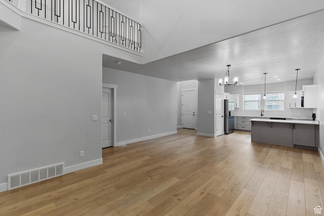 unfurnished living room with a chandelier, light wood-style floors, baseboards, a sink, and a towering ceiling