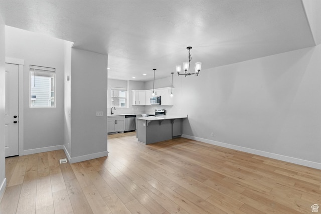 kitchen featuring stainless steel appliances, a sink, a chandelier, a peninsula, and light countertops