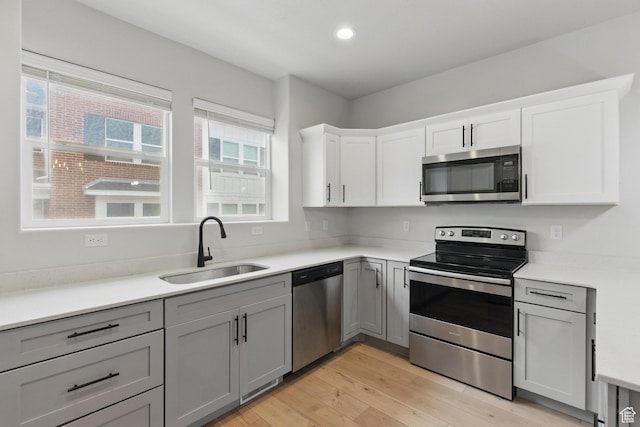 kitchen featuring stainless steel appliances, a sink, gray cabinets, light wood-style flooring, and recessed lighting