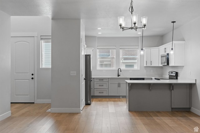 kitchen with stainless steel appliances, a sink, a peninsula, gray cabinets, and light wood finished floors