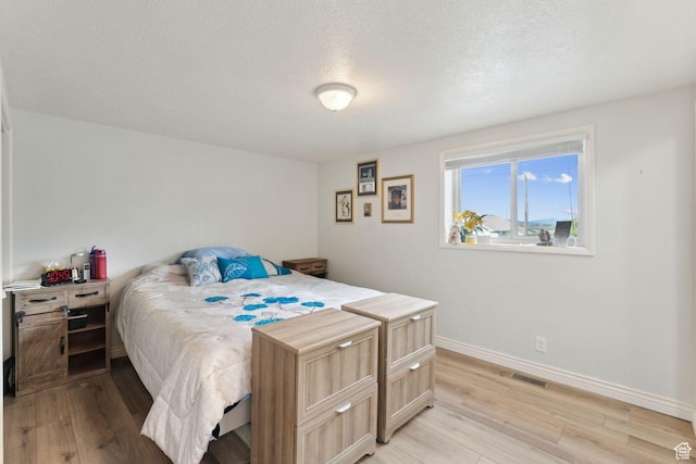 bedroom with light wood finished floors, baseboards, and a textured ceiling