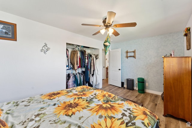 bedroom featuring wood finished floors, a closet, baseboards, a ceiling fan, and wallpapered walls
