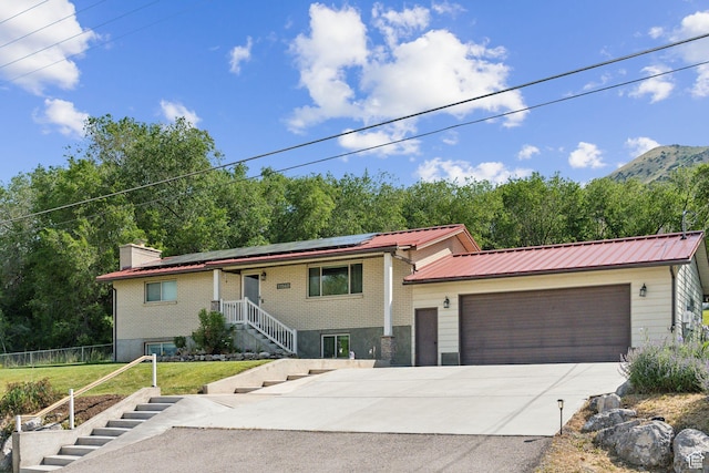 view of front of property with driveway, solar panels, an attached garage, metal roof, and stairway