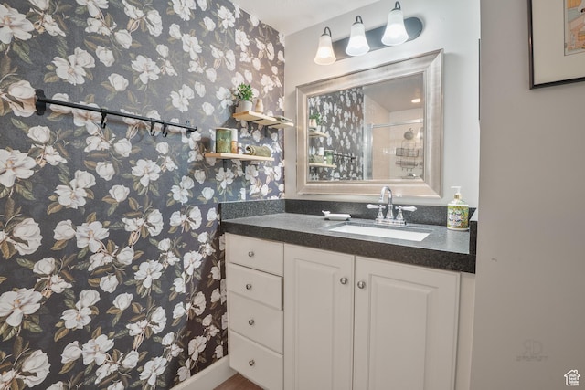 bathroom featuring wallpapered walls, a shower stall, and vanity