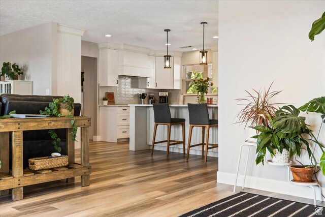 851 E Posado St, Ivins, UT 84738 - kitchen with custom exhaust hood, a kitchen bar, light wood-style floors, white cabinetry, and backsplash