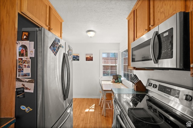 kitchen featuring stainless steel appliances, light wood-style flooring, a textured ceiling, baseboards, and brown cabinetry