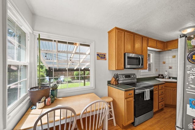 kitchen featuring appliances with stainless steel finishes, light wood finished floors, a sink, brown cabinets, and dark countertops
