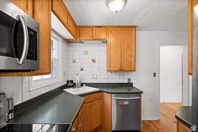 kitchen featuring stainless steel appliances, a sink, dark countertops, backsplash, and light wood-style flooring