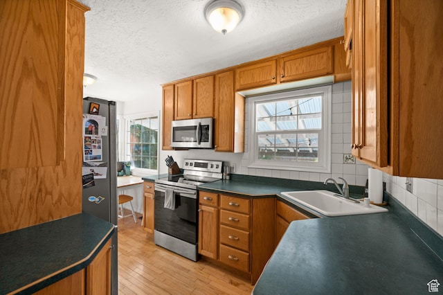 kitchen with stainless steel appliances, a sink, a textured ceiling, brown cabinets, and dark countertops