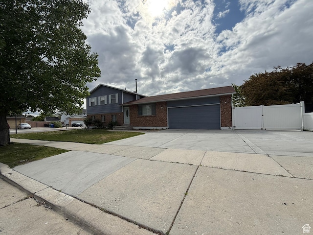 6351 S Moki Cir W, West Jordan, UT 84081 - split level home with concrete driveway, an attached garage, brick siding, a gate, and fence