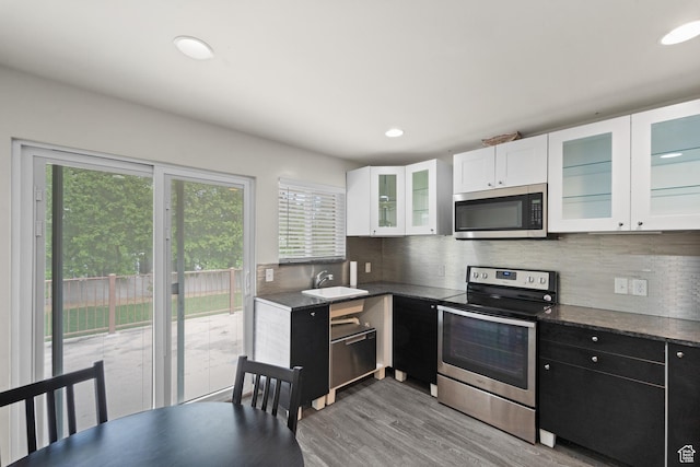 kitchen featuring stainless steel appliances, dark countertops, white cabinetry, backsplash, and light wood-type flooring