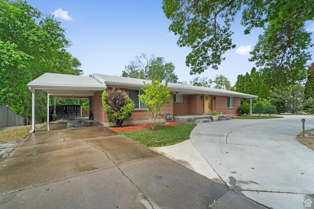 ranch-style home featuring concrete driveway, an attached carport, and brick siding