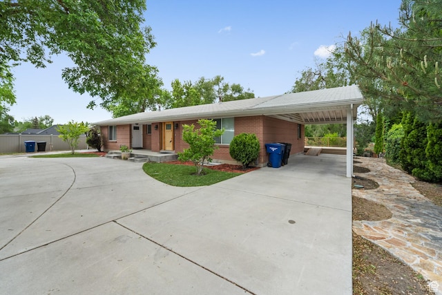 single story home featuring driveway, brick siding, an attached carport, and fence