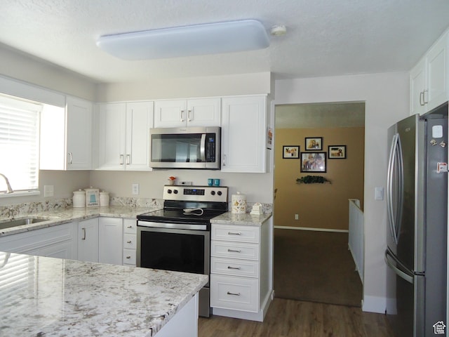 kitchen featuring stainless steel appliances, a sink, white cabinets, dark wood-style floors, and light stone countertops