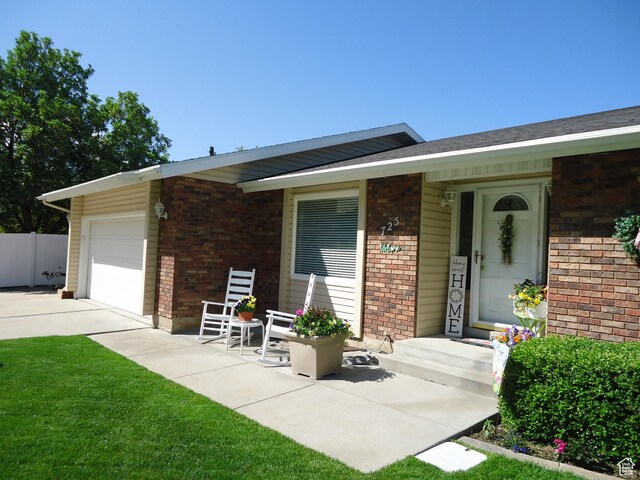 view of exterior entry featuring brick siding, an attached garage, concrete driveway, and fence