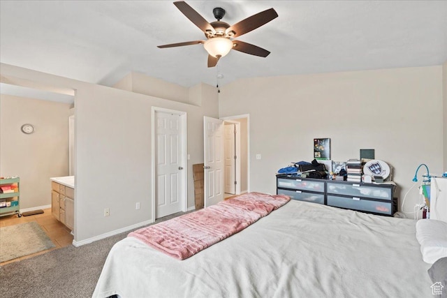 bedroom featuring light carpet, baseboards, a ceiling fan, and ensuite bath