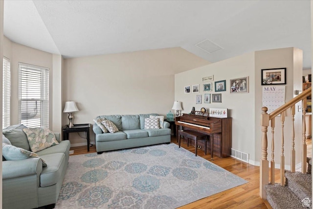 living area with wood finished floors, stairs, baseboards, and vaulted ceiling