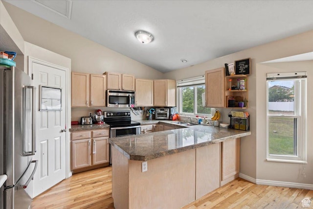 kitchen with stainless steel appliances, light brown cabinets, a peninsula, light wood finished floors, and a sink