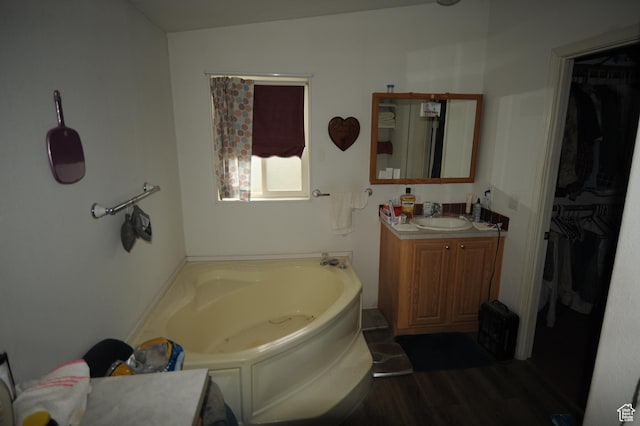 bathroom with a spacious closet, a garden tub, vanity, and wood finished floors