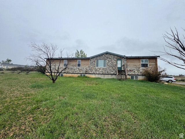 rear view of property featuring entry steps, stone siding, and a yard