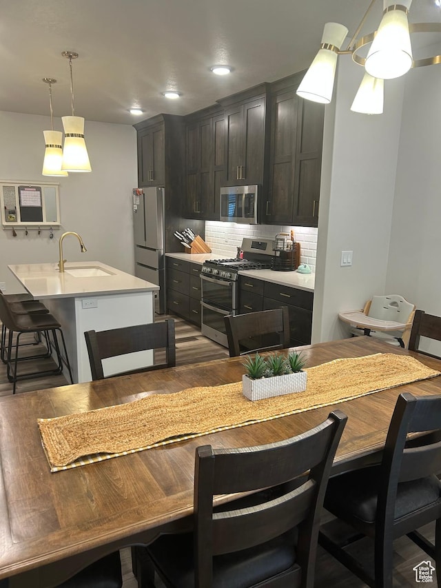 kitchen with appliances with stainless steel finishes, a sink, tasteful backsplash, light countertops, and wood finished floors