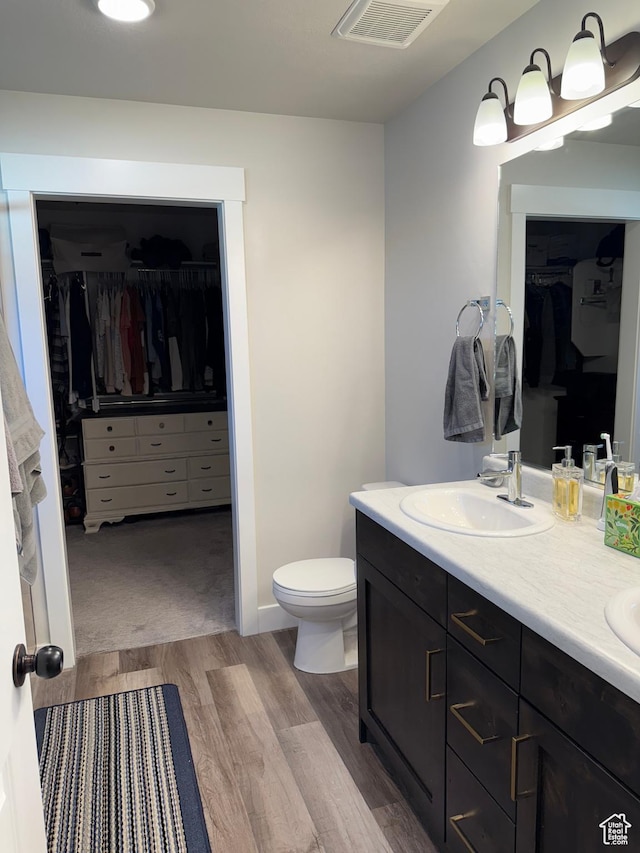 bathroom with a walk in closet, wood finished floors, toilet, and double vanity