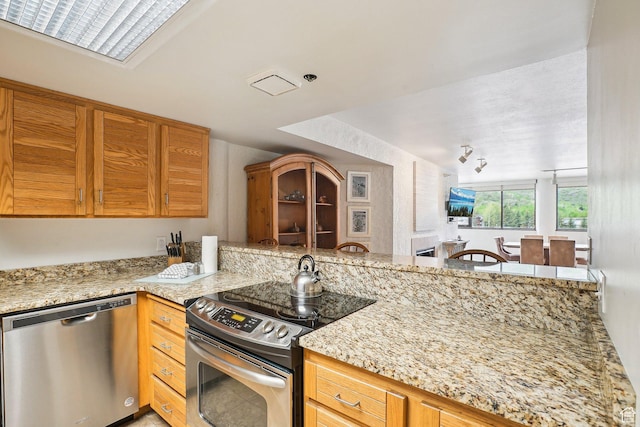 kitchen featuring stainless steel appliances, light stone countertops, a peninsula, and track lighting