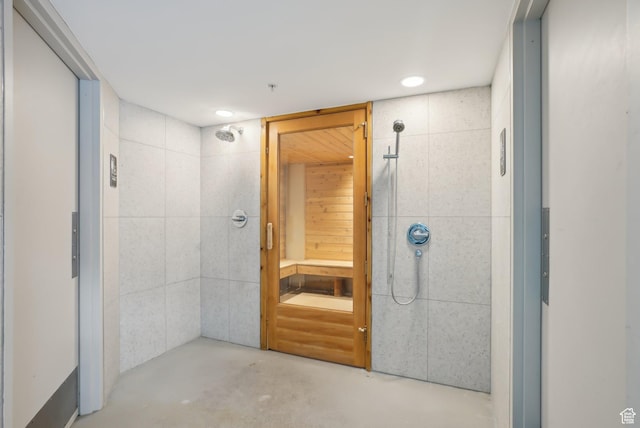 full bathroom with concrete floors, tiled shower, recessed lighting, elevator, and tile walls