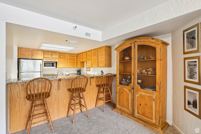kitchen featuring appliances with stainless steel finishes, light stone counters, carpet flooring, a peninsula, and a textured wall