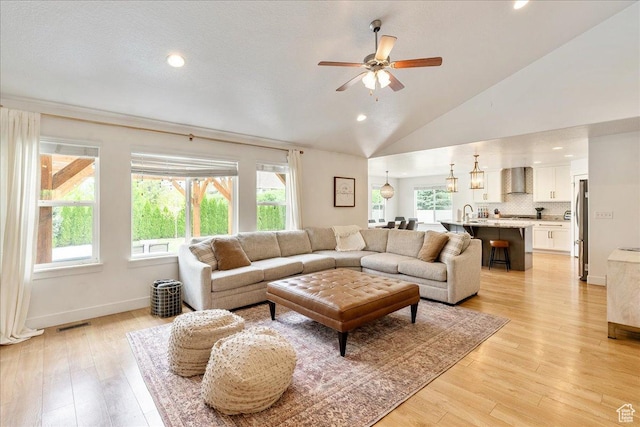 living room with plenty of natural light, ceiling fan, vaulted ceiling, light wood-type flooring, and recessed lighting