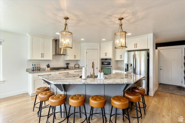 kitchen featuring wall chimney exhaust hood, appliances with stainless steel finishes, a sink, baseboards, and white cabinets