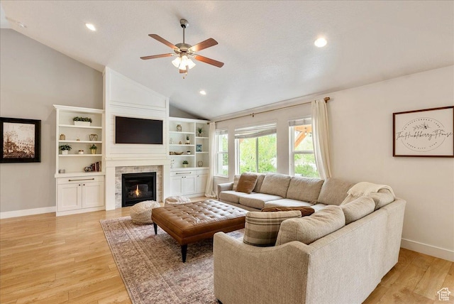 living area featuring lofted ceiling, a ceiling fan, baseboards, light wood-type flooring, and a large fireplace