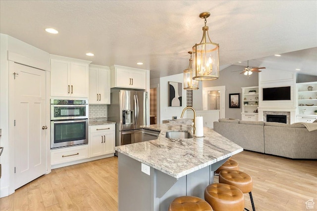 kitchen with stainless steel appliances, a sink, lofted ceiling, light wood finished floors, and white cabinetry