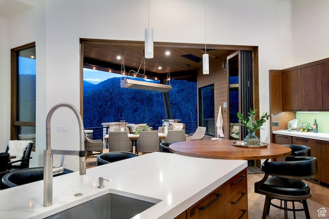 kitchen with a sink, modern cabinets, light countertops, decorative light fixtures, and brown cabinets