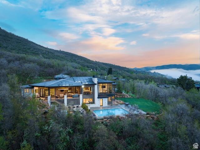 back of property featuring a mountain view, an outdoor pool, a patio area, a balcony, and a wooded view