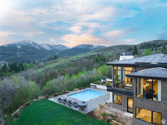 outdoor pool featuring a mountain view, a patio area, and a lawn