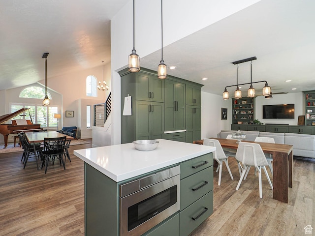 kitchen with green cabinetry, stainless steel microwave, open floor plan, light wood-style floors, and vaulted ceiling
