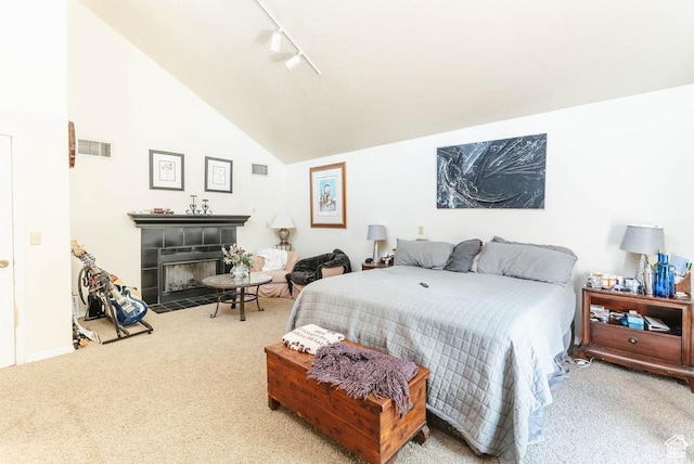 bedroom with carpet floors, a tile fireplace, rail lighting, and lofted ceiling