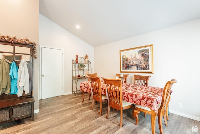 dining room with light wood finished floors, baseboards, and high vaulted ceiling