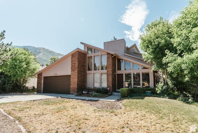 mid-century inspired home featuring concrete driveway, a chimney, an attached garage, a front yard, and a mountain view