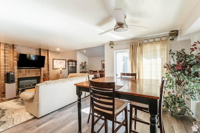 dining room featuring light wood-style flooring, a ceiling fan, a brick fireplace, and recessed lighting