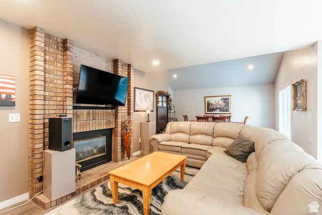 living area with vaulted ceiling, wood finished floors, baseboards, a brick fireplace, and recessed lighting