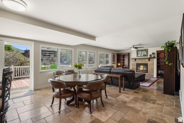 dining room with stone tile flooring, ceiling fan, a high end fireplace, and baseboards