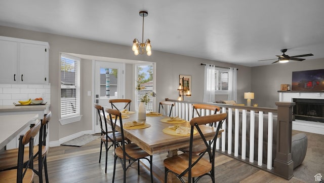 dining area featuring wood finished floors, ceiling fan, a brick fireplace, and a chandelier